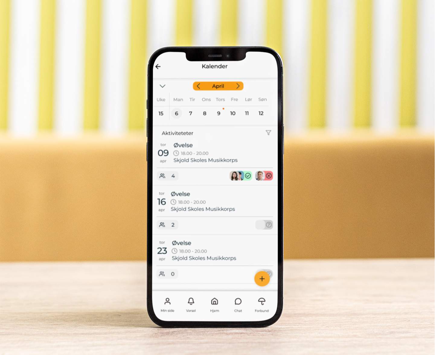 En mobiltelefon som viser kalenderen i Tutti-appen, uskarp bakgrunn med varme farger 